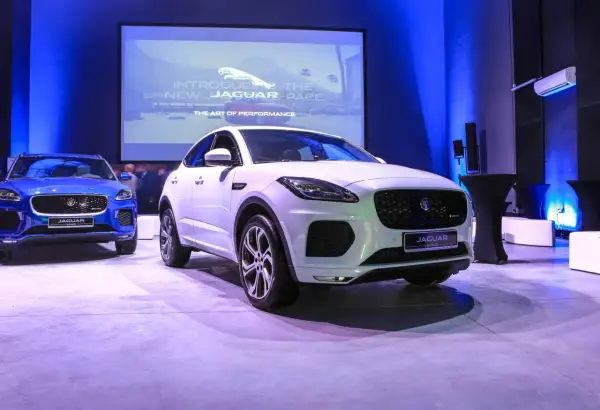 Biały i niebieski Jaguar E-Pace na prezentacji. Na ekranie w tle logo Jaguara i napis "Introducing the new Jaguar E-Pace".