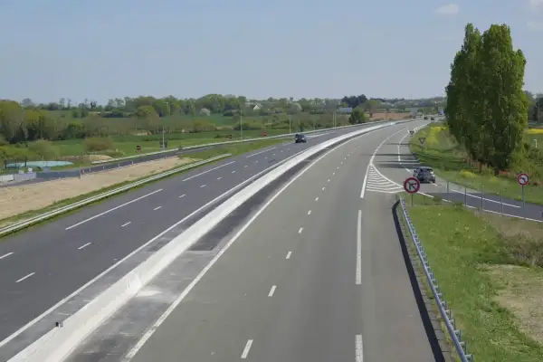 Vue aérienne d'une autoroute avec une voie d'accélération et de décélération, bordée de verdure et de panneaux de signalisation.