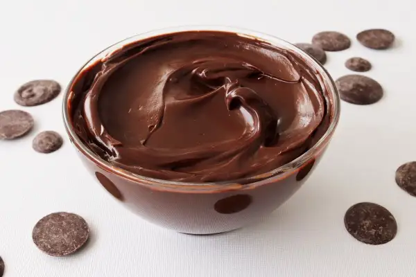 Un tazón de deliciosa crema de chocolate, con trozos de chocolate esparcidos alrededor.