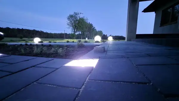 Nocny ogród rozświetlony kulistymi lampami, które tworzą magiczną atmosferę. W kostce brukowej wbudowane są dyskretne ledy, podkreślające ścieżkę.