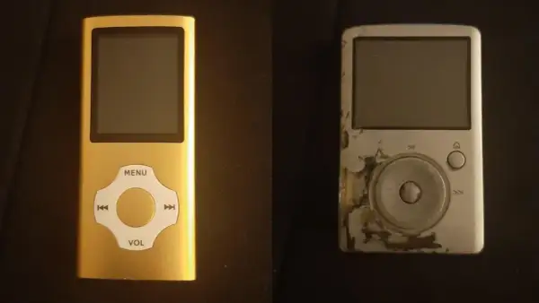 A new gold mp3 player sits next to a worn, scratched silver one.
