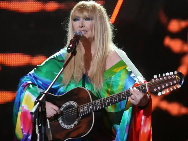 Maryla Rodowicz, ile ma lat, w kolorowym stroju gra na gitarze dwunastostrunowej na scenie.