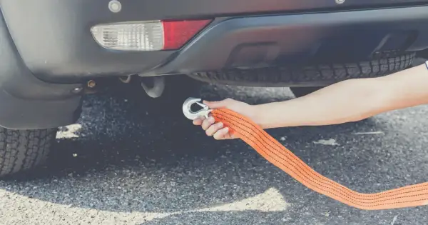 Ręka mocuje hak holowniczy do linki, przygotowując auto do holowania.