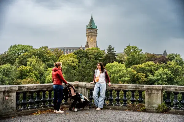 Deux femmes et une poussette devant un bâtiment avec une tour d'horloge, entouré d'arbres.