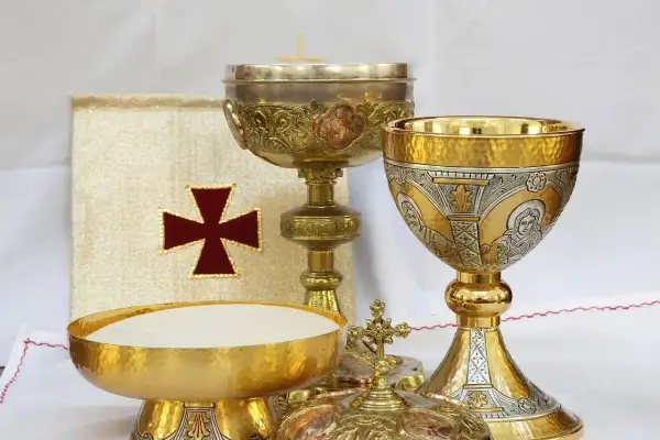 Złoty liturgiczny talerzyk z hostiami, kielichy i księga z krzyżem.