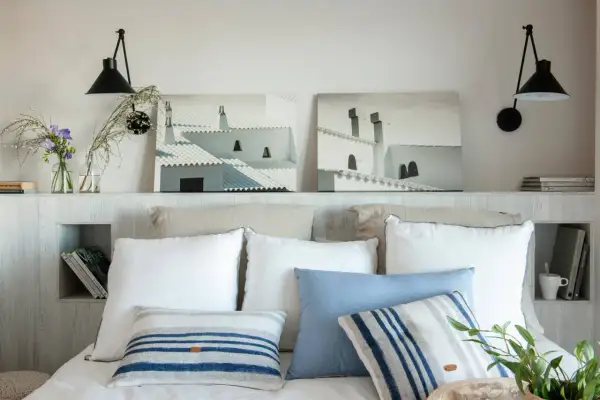 Ideas para hacer un cabecero: dos cuadros de tejados blancos, lámparas negras y cojines a rayas sobre una cama.