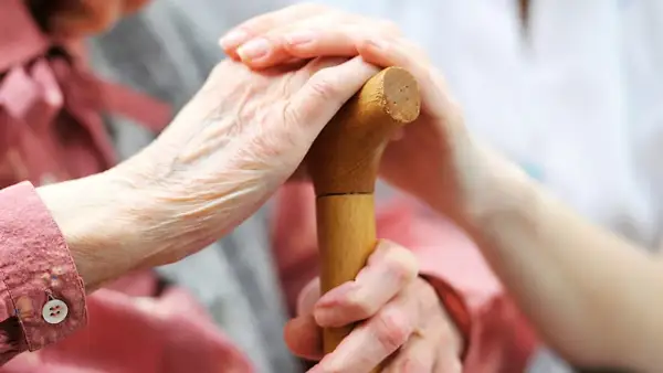 En äldre person håller i en käpp, med en annan hand som stöttar. En **case manager** ger trygghet och hjälp.