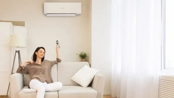 Donna rilassata sul divano, telecomando in mano, con il condizionatore acceso per una perfetta traduzione del comfort.