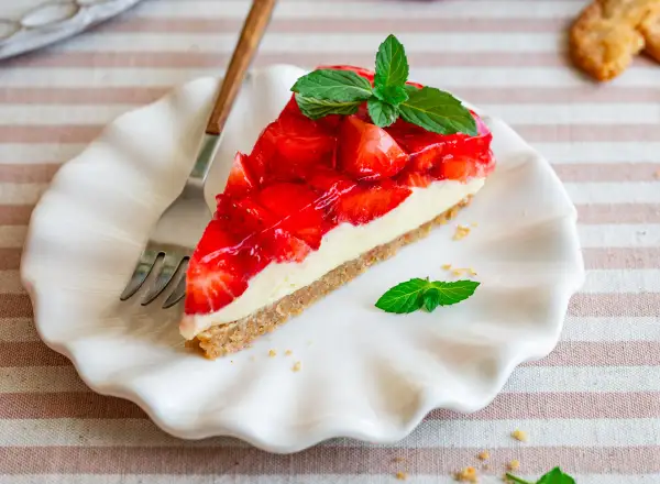 Ein Stück Erdbeer-no-bake-cheesecake mit frischer Minze auf einem weißen Teller, daneben eine Gabel.