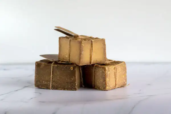 Tres cubos de jabón natural, atados con cuerda rústica, apilados sobre una superficie de mármol.