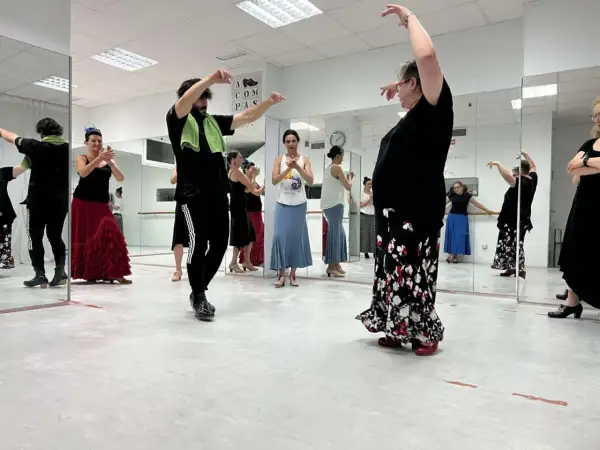 Clase de flamenco facil. Varias personas practican pasos de baile frente a espejos, con movimientos elegantes y faldas amplias.