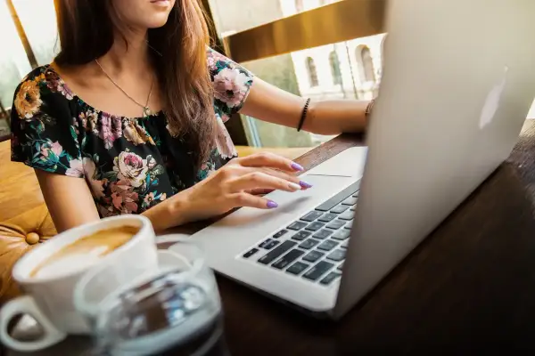 Kobieta z fioletowymi paznokciami pracuje na MacBooku, obok kawa. Nagrywanie ekranu macbooka w kawiarni.