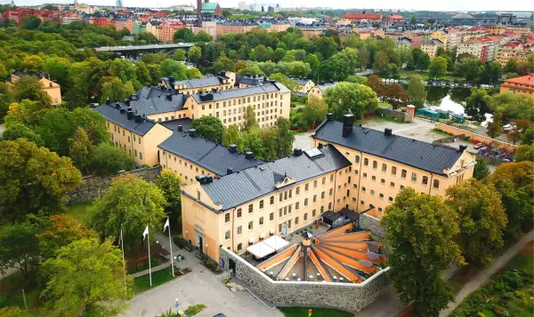 Långholmen vandrarhem, en före detta fängelsebyggnad i Stockholm, omgiven av grönskande träd och med en vacker utsikt över vattnet.