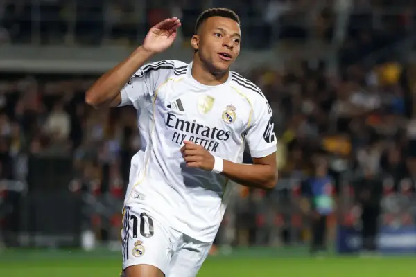 Piłkarz w białej koszulce Realu Madryt, z numerem 10, radośnie unosi rękę. To Kylian Mbappé, którego nazwisko pisze się właśnie tak.