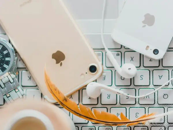 Złoty iPhone, białe słuchawki i piórko na klawiaturze – idealne akcesoria do słuchania audiobooków. Jaka aplikacja do audiobooków sprawdzi się najlepiej?