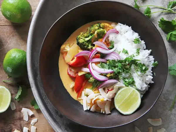 En skål med klimatsmart mat: ris, broccoli, paprika, rödlök och kokosflingor i en krämig currysås, toppad med lime och koriander.