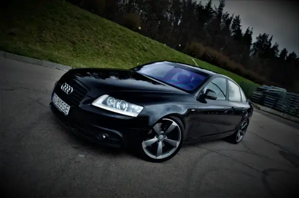 Czarny Audi A6 C6 3.0 TDI Quattro S-line na tle zielonego wzgórza i lasu.