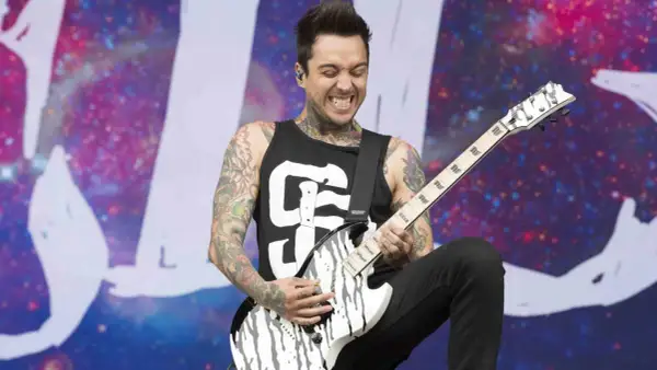A tattooed guitarist, Tony Pierce the Veil, shreds on a white and black guitar on stage with a cosmic backdrop.