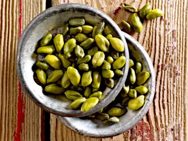 Grüne Pistazienkerne in zwei Schalen auf Holzuntergrund. Sie sind ein gesunder Snack, der viele Nährstoffe liefert.