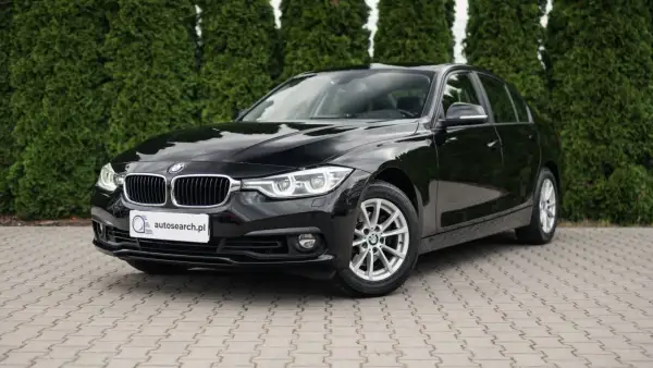 Lśniące czarne BMW 318i stoi na kostce brukowej przed żywopłotem.