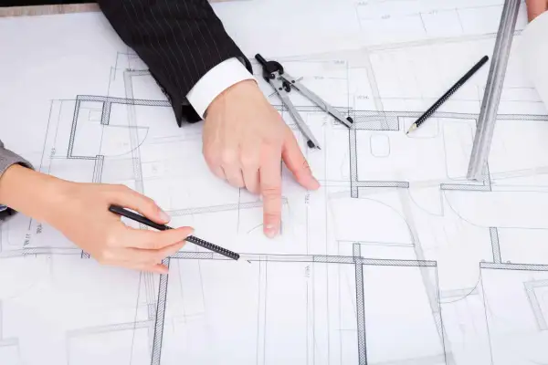 Rysunek techniczny, plan budynku, dyskusja nad projektem zgodnym z art. 36a prawo budowlane. Dłonie wskazują na szczegóły.