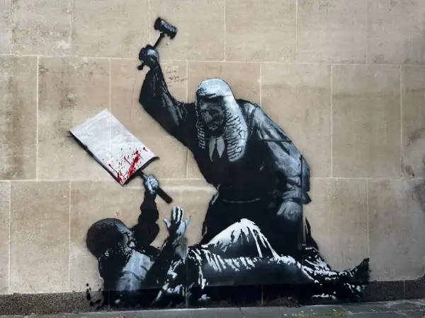 A judge wielding a gavel over a fallen figure, a signature piece by Banksy, questioning justice.