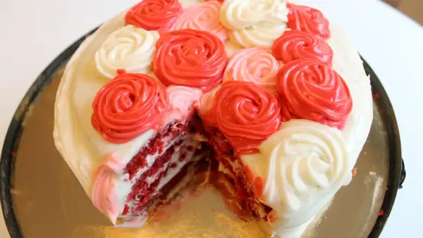 En skivad red velvet cake med vit frosting och dekorationer i form av röda och rosa rosor.