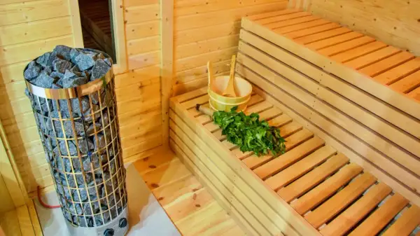 Interno di una sauna fai da te con stufa in pietra, panche in legno, secchiello e frusta di betulla pronti per un relax rigenerante.