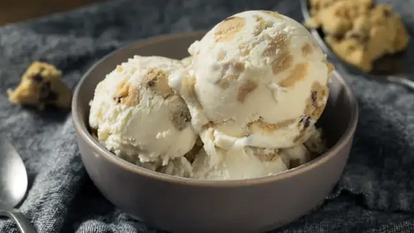 Schüssel mit cremigem Eis, durchzogen von Stückchen aus süßem Keksteig und Schokoladenstückchen. Ein Löffel liegt daneben.