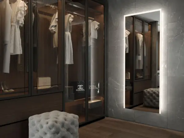 En spegel med belysning bakom spegel ger ett mjukt ljus i en lyxig walk-in-closet med kläder och accessoarer.