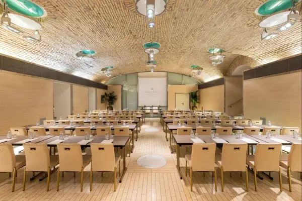 Sala riunioni con tavoli e sedie disposti per un evento all'Anantara Palazzo Naiadi Rome Hotel. Soffitto a volta in mattoni e illuminazione moderna.