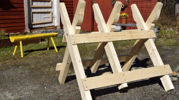 En nybyggd sågbock ritning i trä, redo för vedhuggning. En gul bänk syns i bakgrunden.