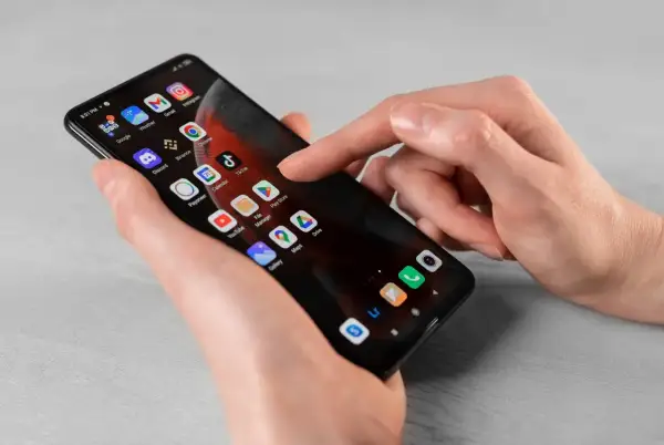 Dłoń dotyka ekranu smartfona z ikonami aplikacji. Dowiedz się, jak usunąć subskrypcję z telefonu, przeglądając ustawienia lub aplikacje.
