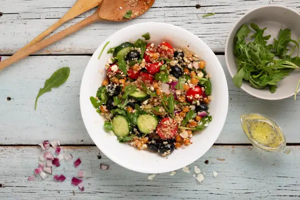 Insalata di quinoa colorata con ceci, pomodorini, olive, cetrioli e rucola. Un piatto fresco e salutare.