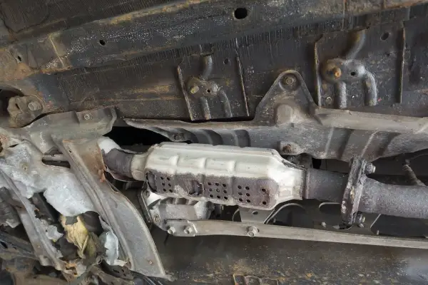 Vue du dessous d'une voiture montrant un catalyseur rouillé, nécessitant un nettoyage catalyseur pour améliorer les performances.