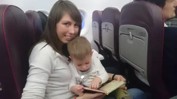 Mama z dzieckiem w samolocie Wizzair. Dziecko przegląda książeczkę, siedząc na kolanach mamy.