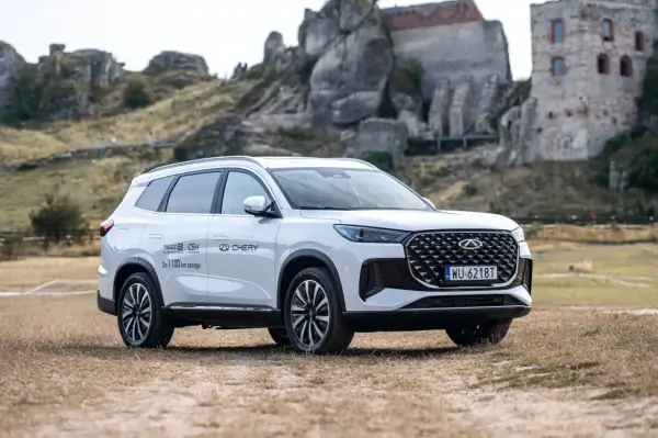 Biały Chery Tiggo 8 Plug-in Hybrid z zasięgiem do 1100 km, zaparkowany na tle ruin zamku. Sprawdź jego cenę!