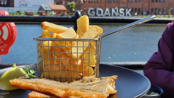 Ryba z frytkami na talerzu, w tle napis GDAŃSK. Idealne miejsce, gdzie zjeść w Gdańsku.