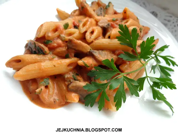 Penne z kremowym sosem pomidorowym i pieczarkami, udekorowane natką pietruszki. Pyszny makaron z pieczarkami.