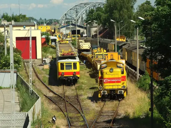 Dwie żółte lokomotywy, jedna z napisem "PKP Energetyka", stoją na torach w słoneczny dzień.
