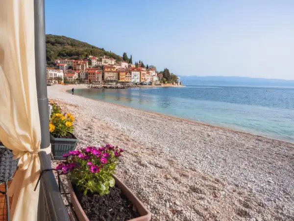 Kamienista plaża z widokiem na kolorowe domki na wzgórzu. To właśnie takie widoki sprawiają, że Istria ma najpiękniejsze plaże.