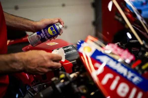 Mani che usano WD-40 per lucidare la plastica di una moto da corsa rossa, per un look brillante.