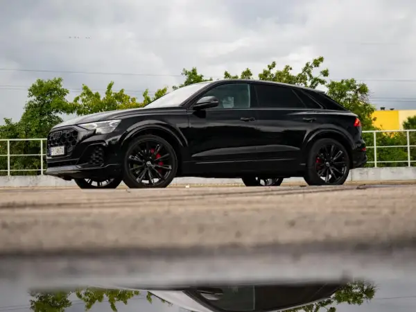Czarny Audi Q9 z czerwonymi zaciskami hamulcowymi, odbijający się w kałuży. Sprawdź audi q9 cena!