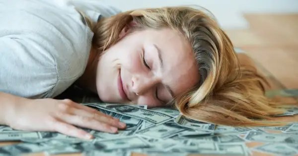 Uśmiechnięta kobieta śpi na stosie banknotów dolarowych. Marzy o tym, czy polskie gwiazdy rzeczywiście biorą udział w międzynarodowych kumulacjach.
