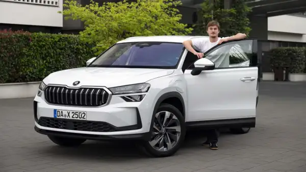 En ung man lutar sig mot en vit Skoda Kodiaq med öppen dörr. En spännande skoda kodiaq test.