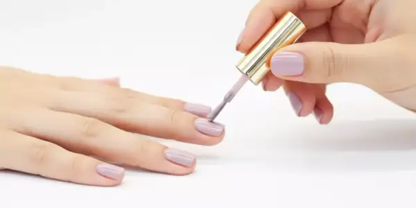 Applicazione smalto lilla su unghie. Il tempo asciugatura vernice smalto è fondamentale per un risultato perfetto.