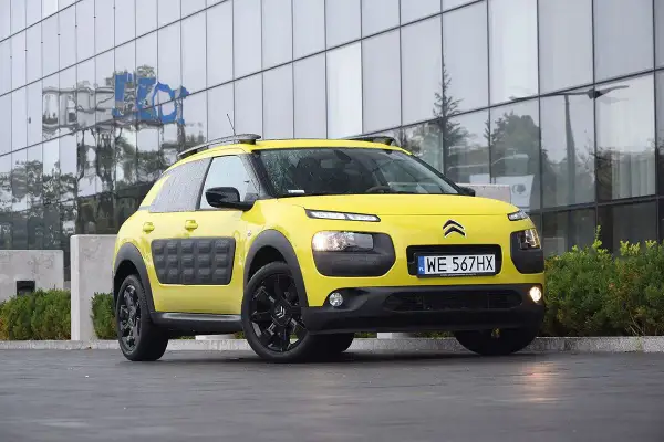 Żółty Citroen C3 Cactus z czarnymi felgami i charakterystycznymi panelami Airbump stoi przed nowoczesnym budynkiem.