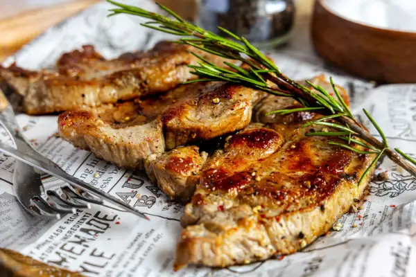 Saftiges Nackensteak im Backofen, perfekt gewürzt und mit Rosmarin garniert, liegt auf Zeitungspapier.