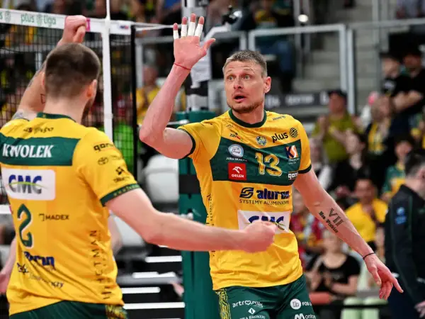 Jurij Gładyr, siatkarz w żółtej koszulce z numerem 13, unosi dłoń z białymi plastrami.