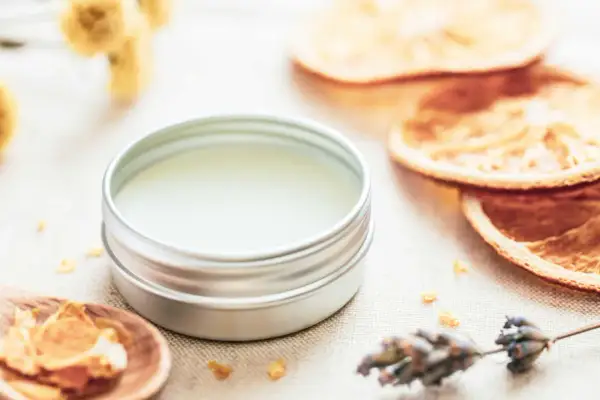 Ein Döschen mit selbstgemachtem Lippenbalsam, umgeben von getrockneten Orangen, Lavendel und Kräutern.